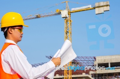 The Young Engineer Holds The Blueprint Over Building Being Built… Stock Photo