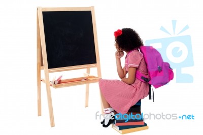 Thoughtful Kid Sitting In Front Of Blackboard Stock Photo