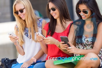 Three Girls Chatting With Their Smartphones At The Campus Stock Photo