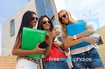 Three Girls Chatting With Their Smartphones At The Campus Stock Photo