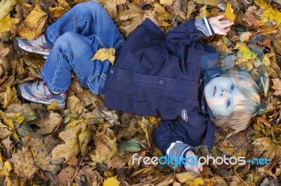 Toddler Blond Boy With Blue Eyes Lays On Bed Of Autumn Fallen Le… Stock Photo