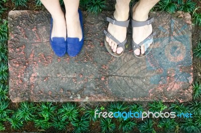 Top View Feet Of Male And Female Couple Lover Standing On Stone Floor Among Little Green Grass Garden. Hipster Style Stock Photo