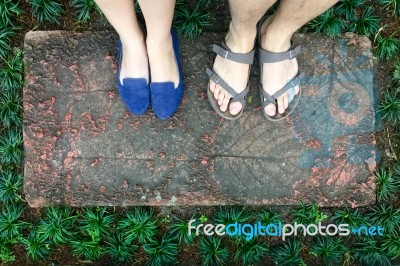 Top View Feet Of Male And Female Couple Lover Standing On Stone Floor Among Little Green Grass Garden. Hipster Style Stock Photo