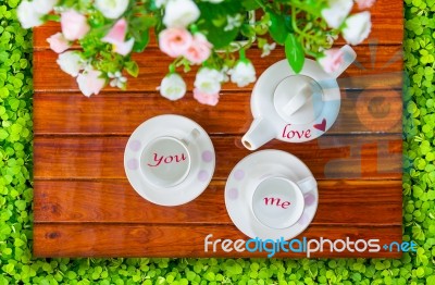 Top View Of The Teapot, Empty  Teacup And Artificial Flowers On A Wooden And Green Stock Photo