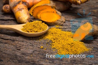 Turmeric Powder In Spoon And Roots On Wooden Plate Stock Photo