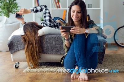 Two Beautiful Young Woman Using Mobile Phone At Home Stock Photo