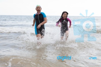 Two Girl Wearing Wet Suit  Playing On Sea Beach With Happiness E… Stock Photo