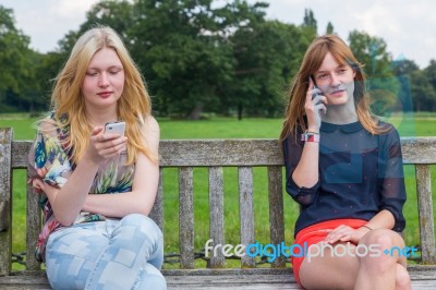 Two Girls On Bench In Park Calling Mobile Stock Photo