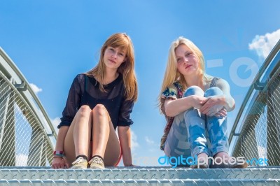 Two Girls Sitting On Metal Bridge With Blue Sky Stock Photo