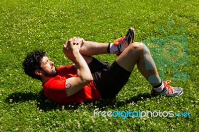 Urban Athlete Doing Stretching Exercises On The Grass Stock Photo