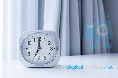 White Square Clock On White Bed Stand With White Curtain Background, Morning Time In Minimal Style Decoration Stock Photo