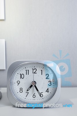 White Square Clock On White Bed Stand With White Wallpaper Background, Morning Time In Minimal Style Decoration Stock Photo