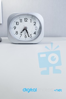 White Square Clock On White Bed Stand With White Wallpaper Background, Morning Time In Minimal Style Decoration Stock Photo