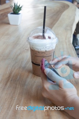 Woman Hand Holding Phone With Background Of Iced Coffee Stock Photo