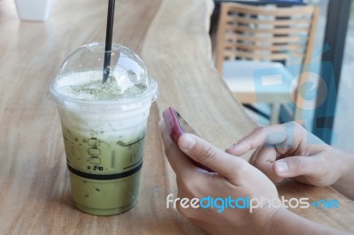 Woman Hand Holding Phone With Background Of Iced Green Tea Stock Photo