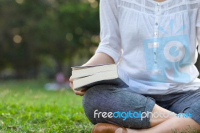 Woman Holding Book And Sitting In Park Stock Photo