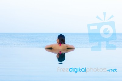 Woman Looking Out From Infinity Swimming Pool Stock Photo