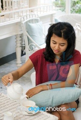 Woman Pouring Tea From The Teapot Into A White Ceramic Cup Stock Photo