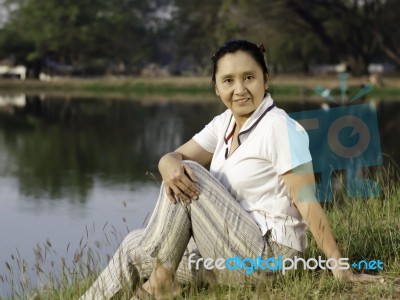 Woman Sitting On Green Field By Lake Stock Photo