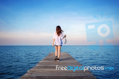 Woman Walking On Wooden Bridge Extended Into The Sea Stock Photo