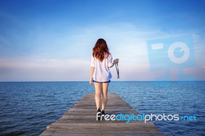 Woman Walking On Wooden Bridge Extended Into The Sea Stock Photo