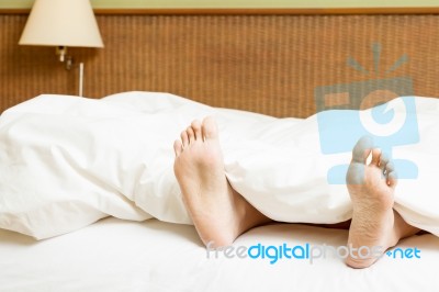 Woman's Feet Sticking Out Of Blanket On Bed At Home Stock Photo