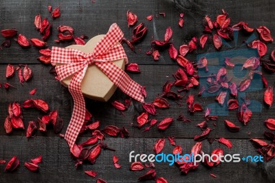 Wrapped Gift  With A Red Bow Surrounded By Dried Petals Stock Photo