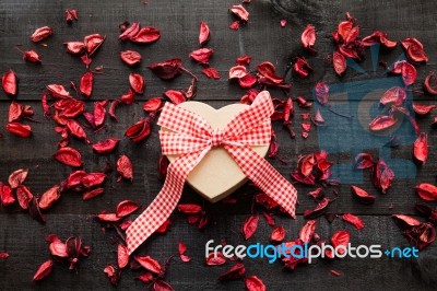 Wrapped Gift  With A Red Bow Surrounded By Dried Petals Stock Photo