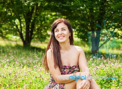 Young Beautiful Smiling Girl Sitting On The Grass Stock Photo