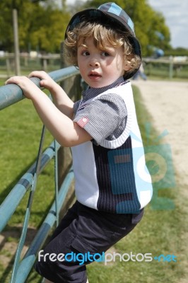 Young Boy With Hat On Climbing On A Gate Stock Photo