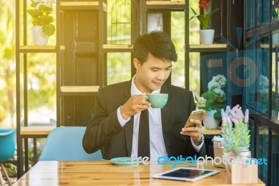 Young Businessmen Are Looking At Mobile Phones And Holding A Cup… Stock Photo