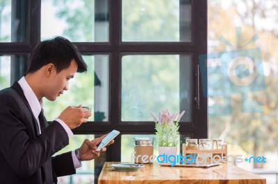 Young Businessmen Are Looking At Mobile Phones And Holding A Cup… Stock Photo