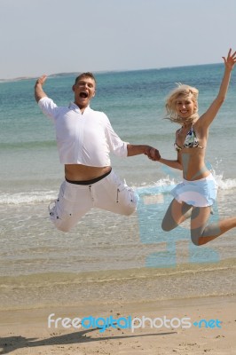 Young Couple Jumping At Beach Stock Photo