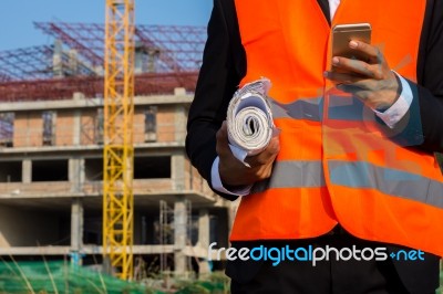 Young Engineer In Orange Shirt Stands Holding A Blueprint And Ta… Stock Photo