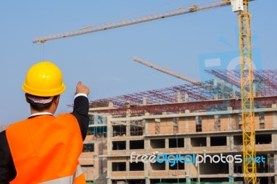 Young Engineer In Orange Shirt Stands Pointing At A Building Bei… Stock Photo