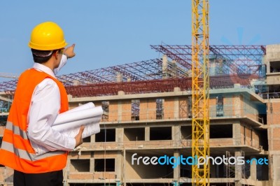 Young Engineer In Orange Shirt Stands Pointing At A Building Bei… Stock Photo