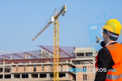 Young Engineer In Orange Shirt Stands Pointing At A Building Bei… Stock Photo