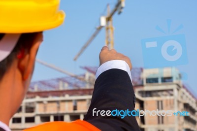 Young Engineer In Orange Shirt Stands Pointing At A Building Bei… Stock Photo