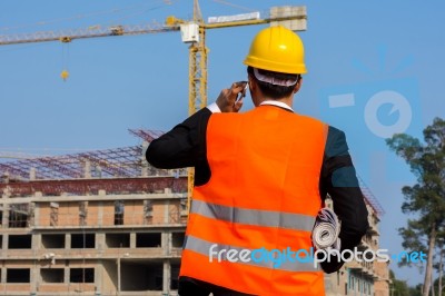 Young Engineer Wearing A Orange Shirt Stands Holding A Blueprint… Stock Photo