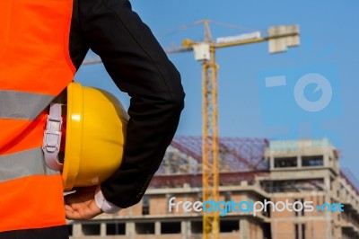 Young Engineer Wearing A Orange Shirt Stands Holding A Hat While… Stock Photo