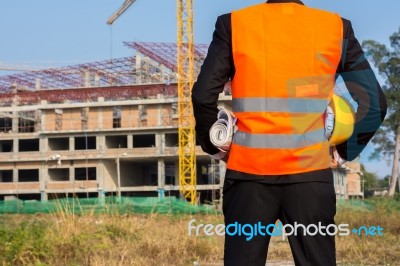 Young Engineer Wearing Orange Shirt Stands Holding A Hat And A B… Stock Photo