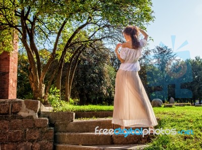 Young Girl In A Light Dress Standing With Her Back In The Park Stock Photo