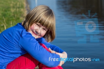 Young Girl Sitting At Waterfront Stock Photo