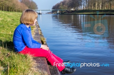 Young Girl Sitting At Waterfront Of Canal Stock Photo