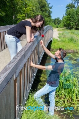 Young Man Offers Red Rose To Attractive Girl On Bridge Stock Photo