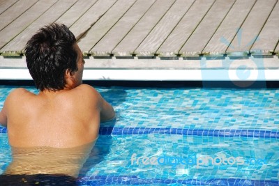 Young Man Relaxing At The Edge Of The Swimming Pool Stock Photo