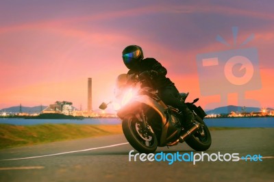 Young Man Riding Sport Touring Motorcycle On Asphalt Highways Against Beautiful Lighting Of Urban Industry Scene Use As Modern People Lifestyle And Holiday Activities Stock Photo