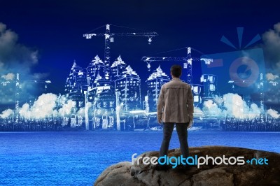 Young Man Standing On Rock And Looking To Building Construction Stock Photo