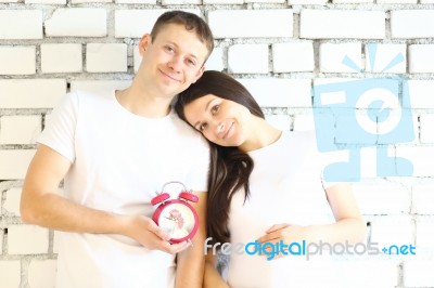 Young Pregnant Woman And Her Husband With Red Alarm Clock Stock Photo