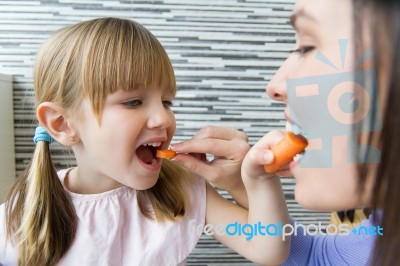 Young Woman And Little Girl Eating Carrots In The Kitchen Stock Photo